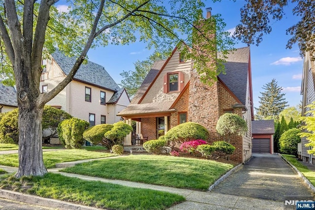 english style home featuring a front lawn, brick siding, a chimney, and a porch