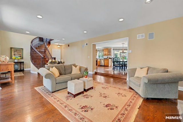 living area with stairs, wood finished floors, visible vents, an inviting chandelier, and baseboards