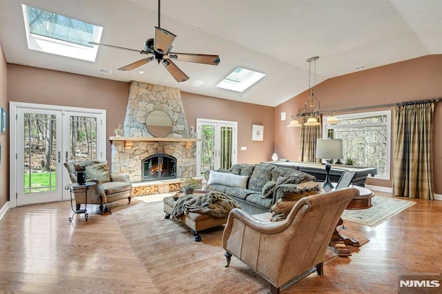 living room with french doors, a healthy amount of sunlight, wood finished floors, and vaulted ceiling with skylight