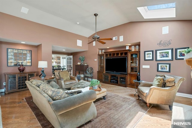 living room featuring a ceiling fan, visible vents, high vaulted ceiling, wood finished floors, and a skylight