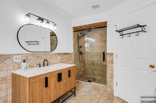 full bath with tile walls, vanity, visible vents, a stall shower, and wainscoting