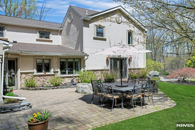 back of house featuring a yard, outdoor dining space, a patio area, stucco siding, and stone siding