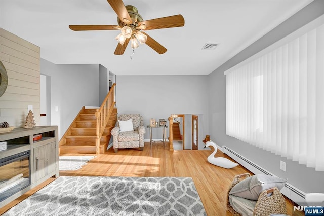 living room featuring wood finished floors, visible vents, a baseboard heating unit, ceiling fan, and stairs