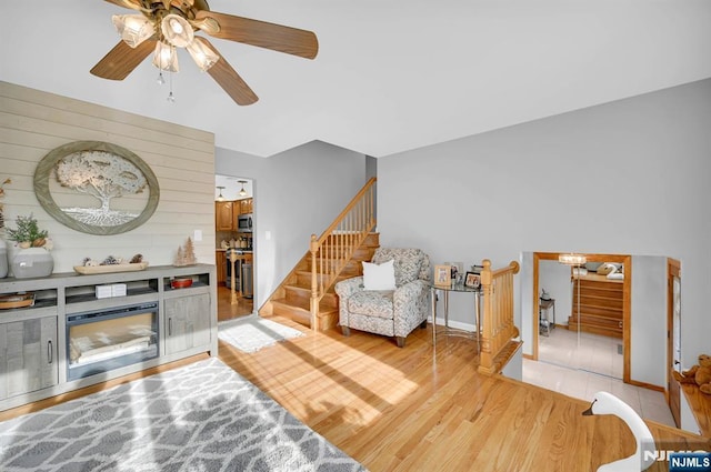 living area featuring light wood-style floors, ceiling fan, and stairs