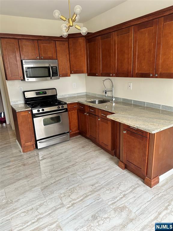 kitchen with stainless steel appliances, a sink, a chandelier, light stone countertops, and decorative light fixtures