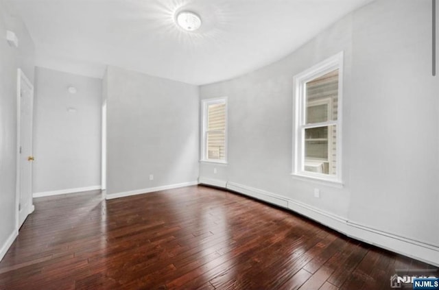 unfurnished room with hardwood / wood-style floors, a baseboard heating unit, and baseboards