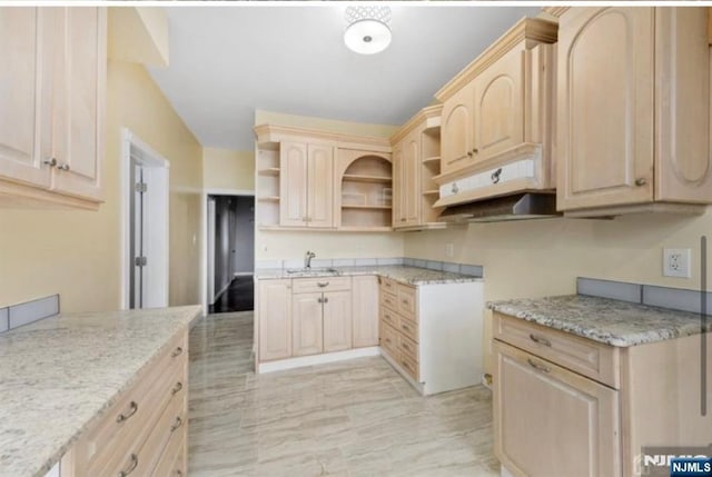 kitchen with open shelves, light brown cabinetry, a sink, and light stone counters