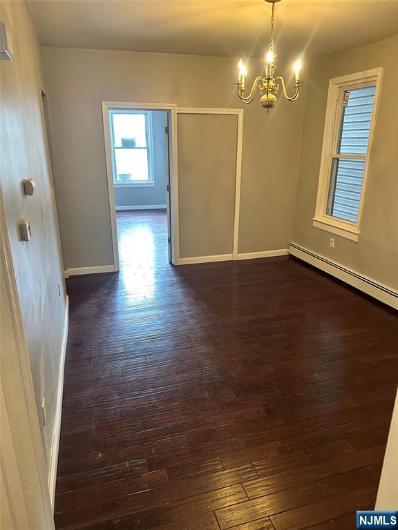 unfurnished dining area with a chandelier, dark wood-style floors, baseboard heating, and baseboards