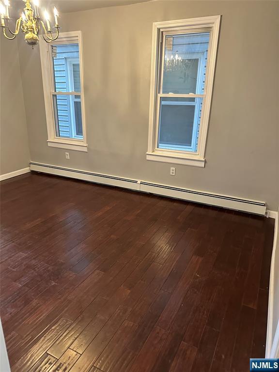spare room with a chandelier, dark wood-style floors, baseboard heating, and baseboards