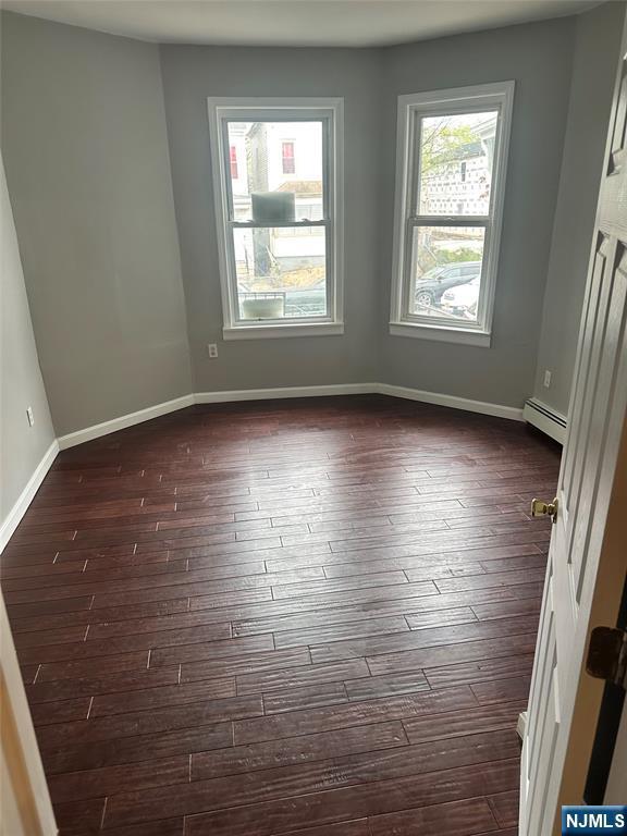 spare room featuring dark wood-type flooring, baseboards, and a baseboard heating unit