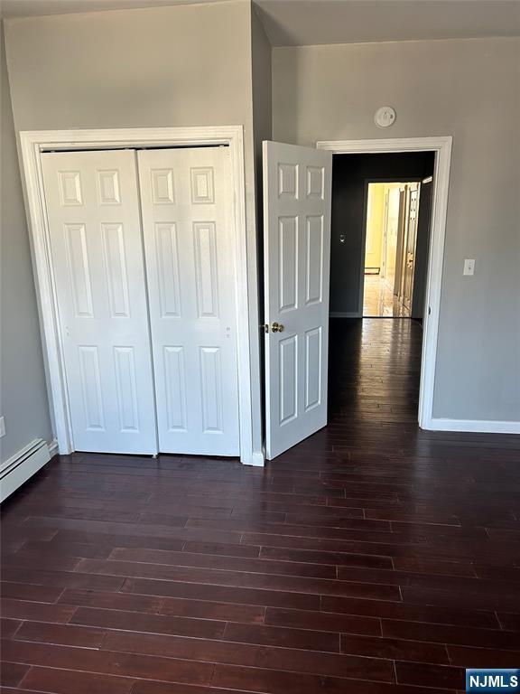 unfurnished bedroom featuring dark wood-style flooring, baseboards, and a closet