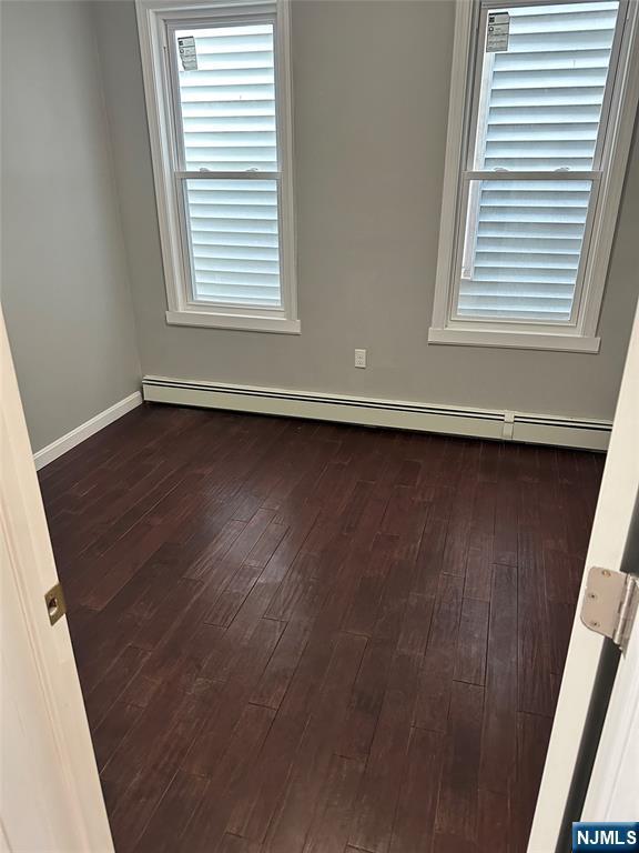 empty room featuring a baseboard radiator, dark wood-style floors, and baseboards