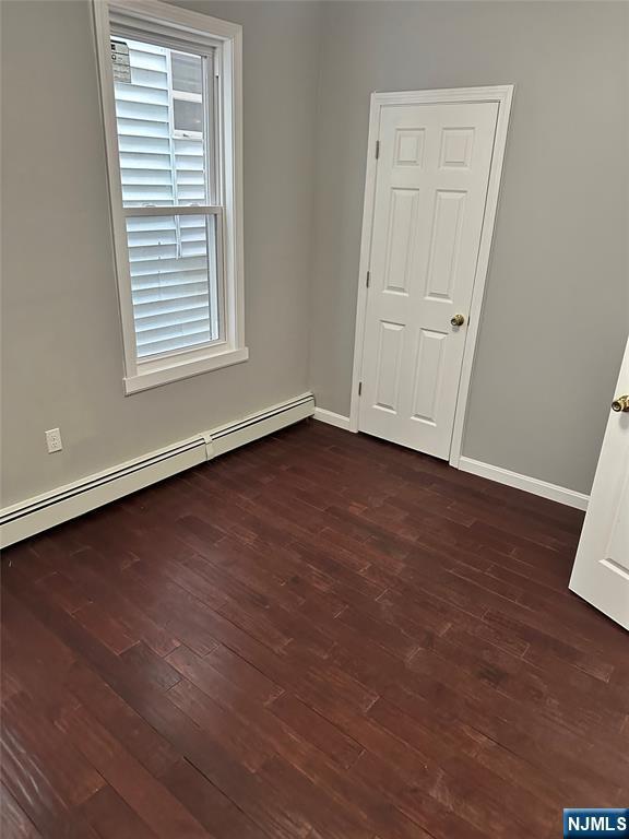 spare room with a baseboard radiator, dark wood-style flooring, and baseboards