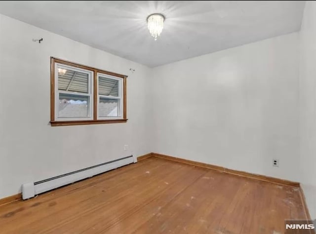 spare room featuring a baseboard radiator, baseboards, and hardwood / wood-style floors