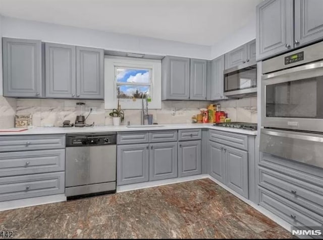 kitchen featuring a sink, a warming drawer, gray cabinetry, appliances with stainless steel finishes, and decorative backsplash