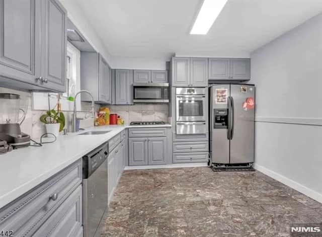 kitchen with a sink, gray cabinets, a warming drawer, appliances with stainless steel finishes, and decorative backsplash