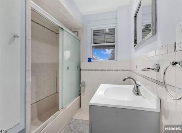 bathroom featuring tile walls, vanity, and shower / bath combination with glass door