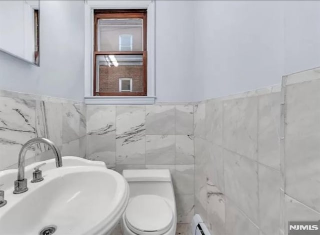 half bathroom featuring a sink, wainscoting, tile walls, and toilet