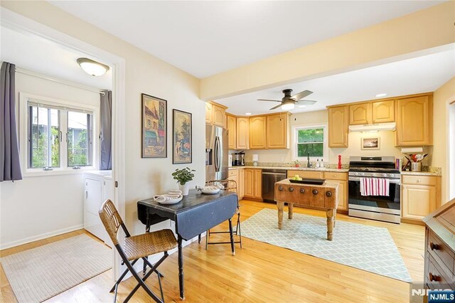 kitchen featuring light wood finished floors, washing machine and clothes dryer, under cabinet range hood, light countertops, and appliances with stainless steel finishes