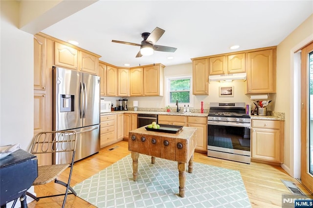 kitchen featuring light wood-style flooring, a sink, light brown cabinetry, under cabinet range hood, and appliances with stainless steel finishes