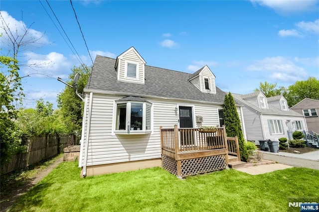back of house featuring fence, roof with shingles, a deck, and a lawn