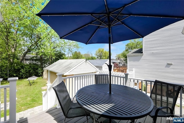 wooden terrace featuring a lawn, an outbuilding, outdoor dining area, and a storage shed