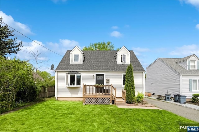 rear view of property with roof with shingles, a wooden deck, fence, and a lawn