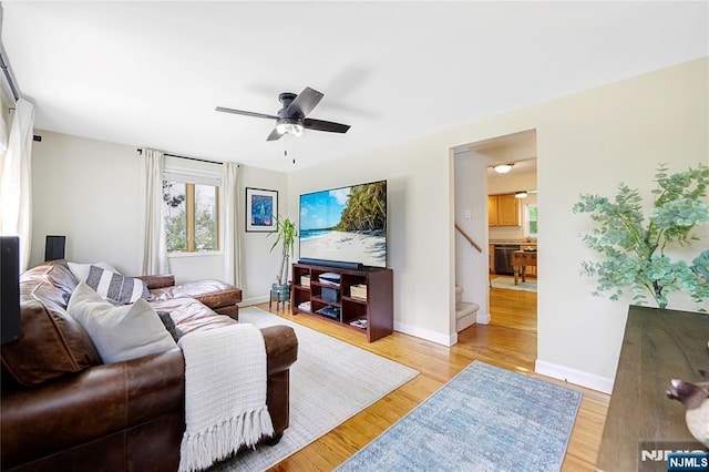 living area featuring ceiling fan, stairs, baseboards, and light wood finished floors