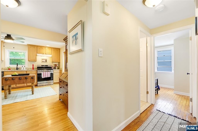 corridor featuring baseboards, light wood finished floors, and a sink