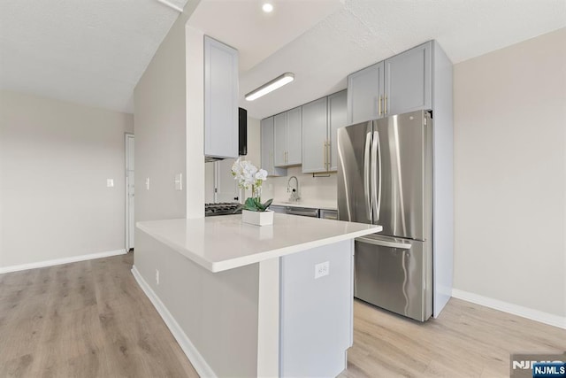 kitchen featuring light wood finished floors, gray cabinetry, light countertops, and stainless steel appliances