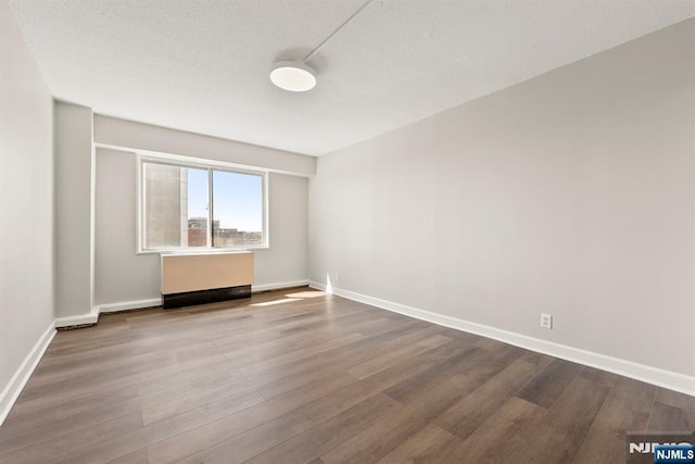 empty room featuring baseboards, dark wood-style flooring, and a textured ceiling