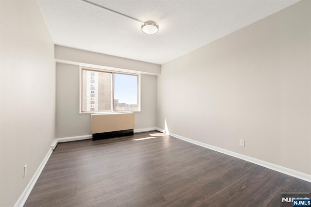 unfurnished room featuring baseboards, radiator, and dark wood-style floors