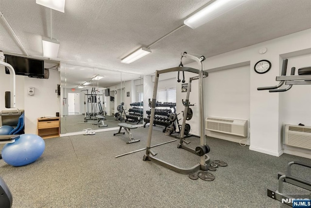 gym featuring a textured ceiling, baseboards, and a wall unit AC