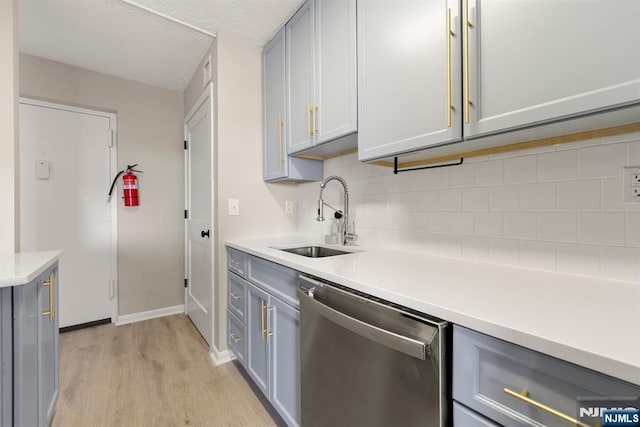 kitchen with light wood finished floors, a sink, stainless steel dishwasher, and gray cabinets