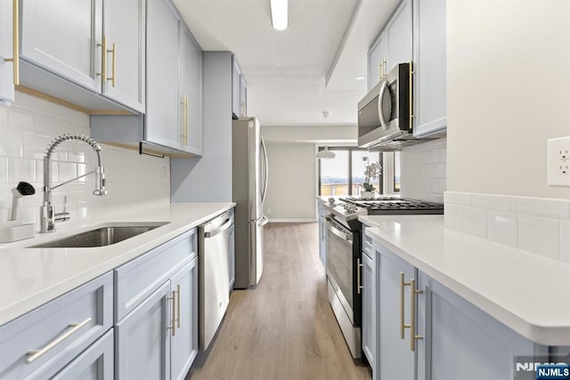 kitchen featuring light countertops, a sink, decorative backsplash, light wood-style floors, and stainless steel appliances