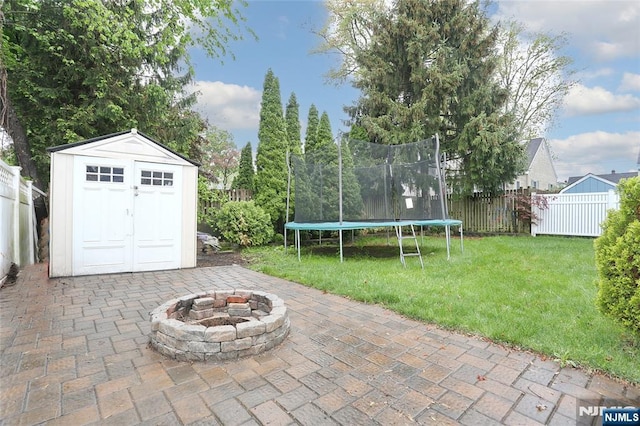 view of patio with a trampoline, a fire pit, a storage unit, and an outbuilding