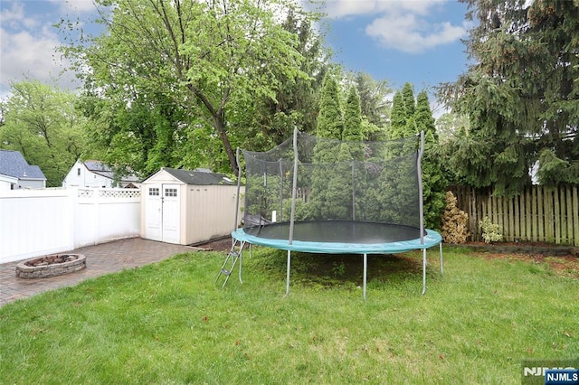view of yard featuring a trampoline, an outdoor fire pit, a shed, an outdoor structure, and a patio