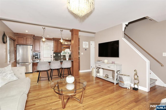 living room with stairway, decorative columns, light wood-style flooring, baseboards, and a chandelier