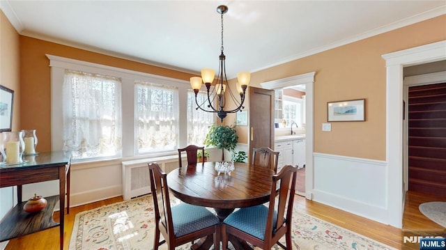 dining room featuring a chandelier, radiator heating unit, light wood-style floors, crown molding, and baseboards
