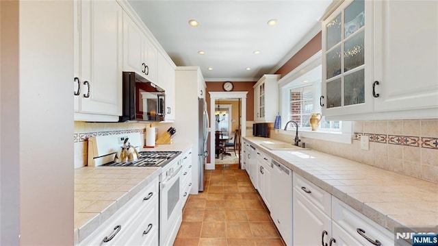 kitchen with white appliances, a sink, tile countertops, white cabinetry, and ornamental molding