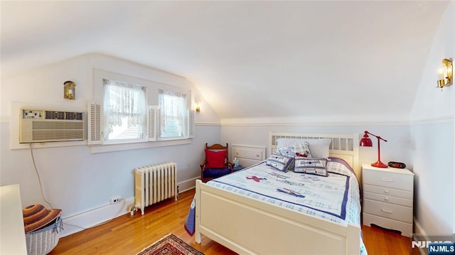 bedroom with radiator heating unit, vaulted ceiling, an AC wall unit, and wood finished floors