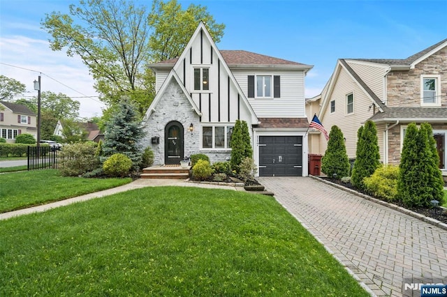 english style home featuring stone siding, an attached garage, decorative driveway, and roof with shingles