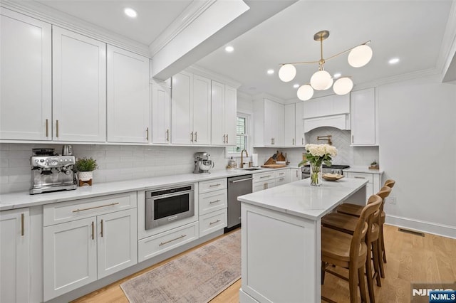 kitchen featuring stainless steel dishwasher, light wood-style flooring, white cabinets, decorative backsplash, and a breakfast bar area
