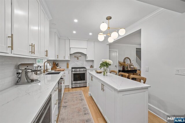 kitchen featuring appliances with stainless steel finishes, a sink, white cabinetry, a center island, and backsplash