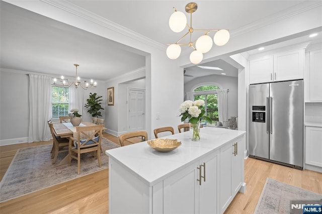 kitchen featuring high quality fridge, a chandelier, white cabinetry, a center island, and light stone countertops