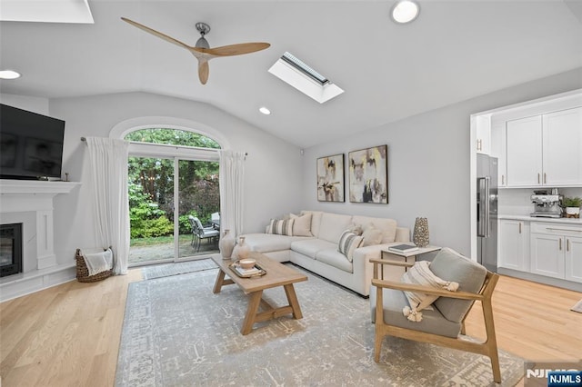 living area with vaulted ceiling, ceiling fan, light wood finished floors, a skylight, and recessed lighting