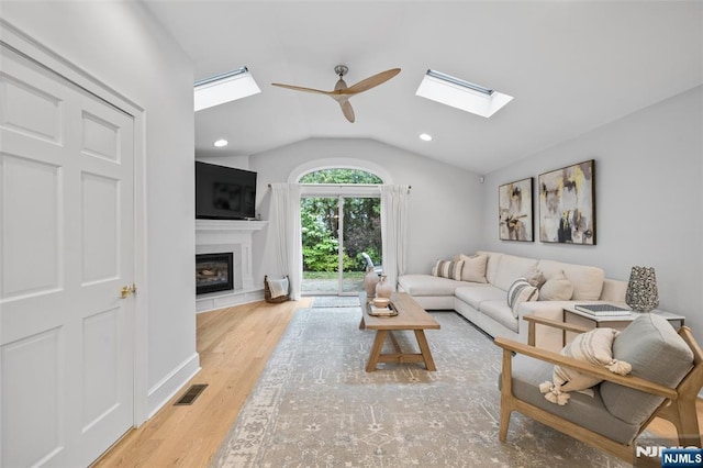 living area with a skylight, lofted ceiling, a ceiling fan, a glass covered fireplace, and wood finished floors