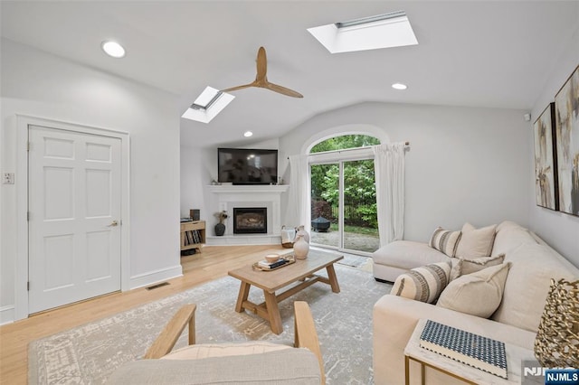 living area with a skylight, wood finished floors, a glass covered fireplace, vaulted ceiling, and recessed lighting