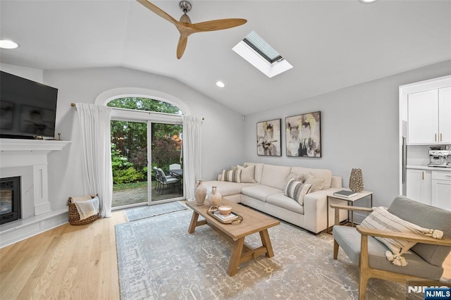 living area featuring vaulted ceiling, ceiling fan, a skylight, light wood-style floors, and recessed lighting