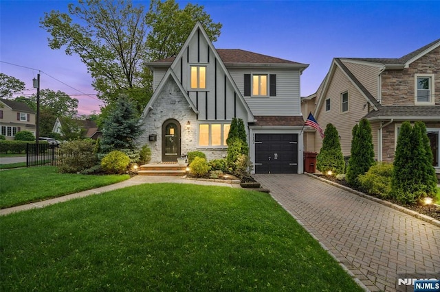 tudor home with an attached garage, stone siding, decorative driveway, and a shingled roof
